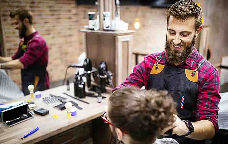 Barbershop owner trimming a customer's beard.
