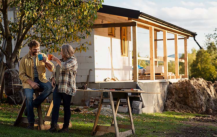 Couple cheers mugs outside a house in construction