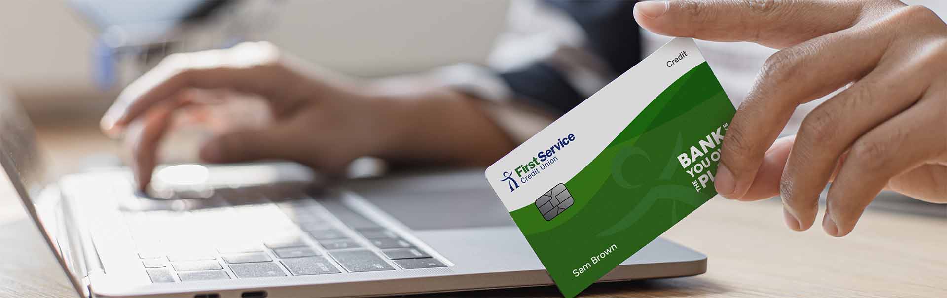 FSCU Credit Card balanced vertically by a hand next to a laptop