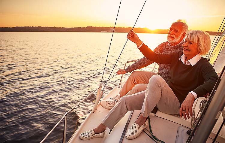 Happy elder couple sitting on boat at sunset